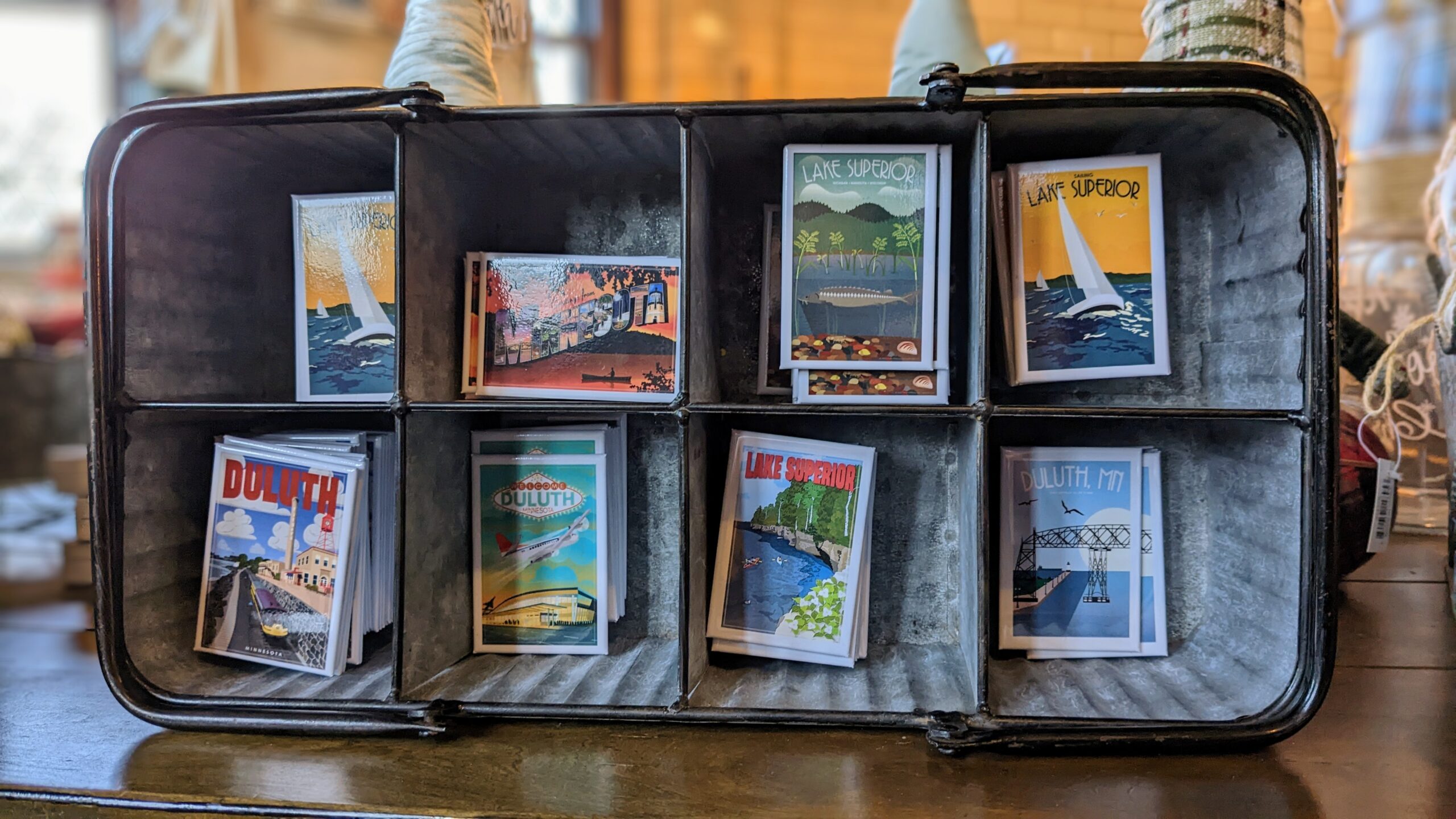 Magnets of various Duluth attractions sit in a metal tin with cubbies on a wooden desk.