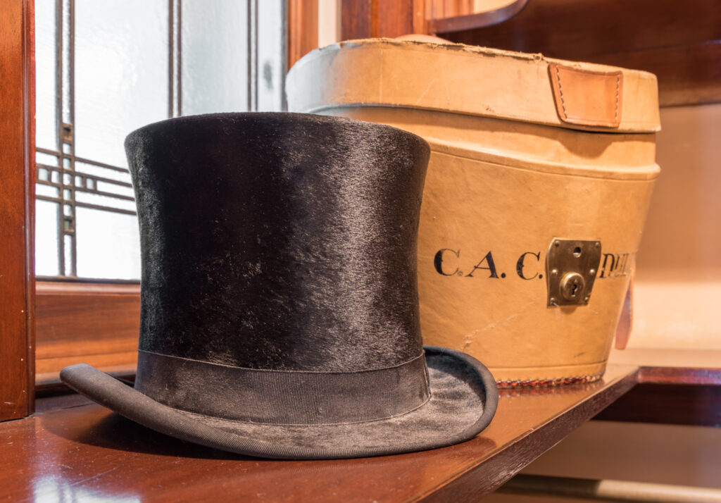 A black top hat sits on a table next to a white box.